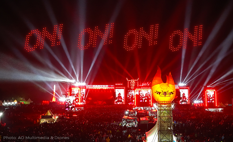 projects_wackenopenair2025_slider_on Red drone lights create four "ON" above the stage of WOA, beams of light crossing the sky